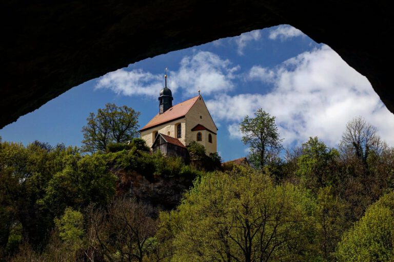 Eine Kapelle auf einem Berg von unten aus einer Höhle heraus fotografiert.