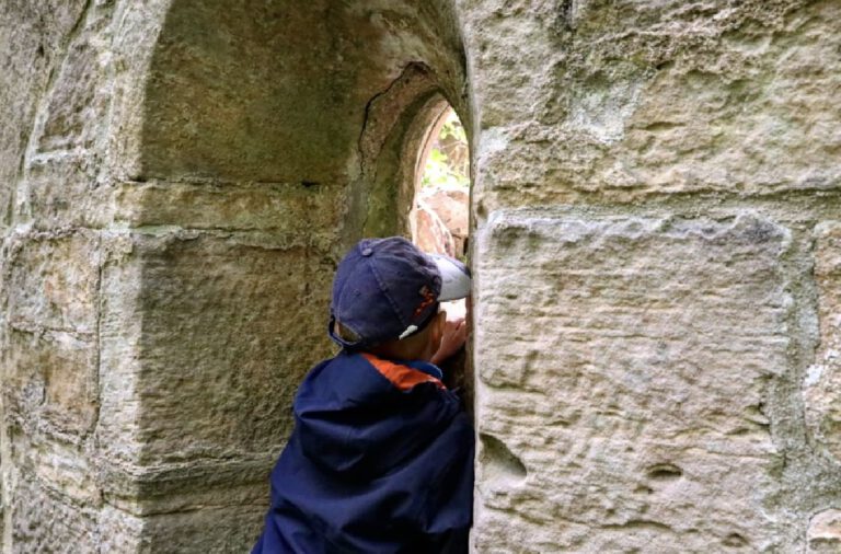 Ein Kind, dass durch einen Spalt einer Burgmauer schaut.