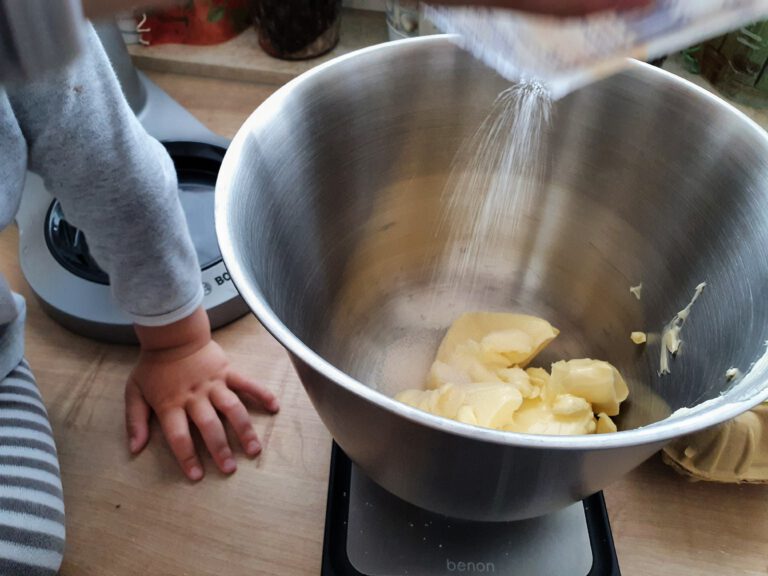 Eine Schüssel mit Butter und eine Kinderhand die etwas hineinschüttet.