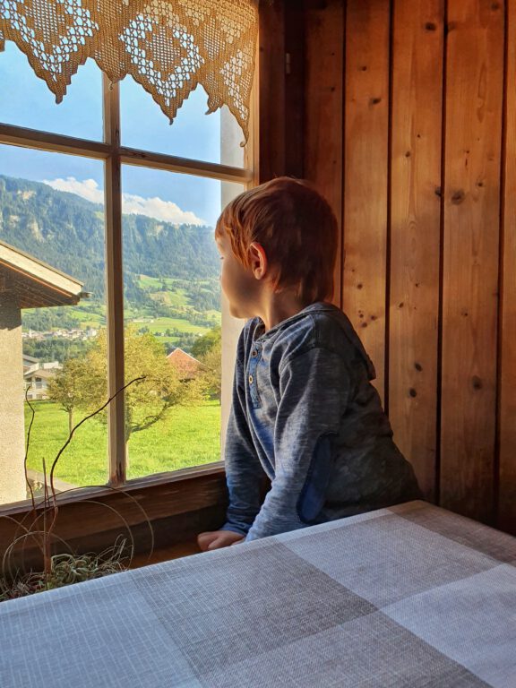 Ein Kind schaut aus dem Fenster in die Berge.