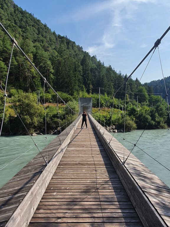 Ich stehe in der Mitte einer Holzhängebrücke. Rechts und links sieht man den blau grünen Rhein.