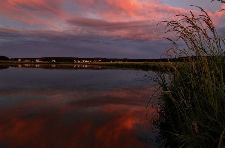 Ein roter Himmel mit Wolken die sich im Weiher spiegeln.