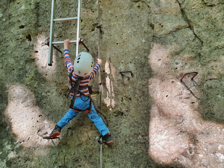 Ein fünfjähriges Kind auf einem Klettersteig. Es versucht auf eine Leiter zu klettern.