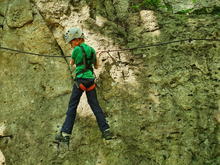 Ein sieben jähriges Kind konzentriert auf einem Klettersteig.