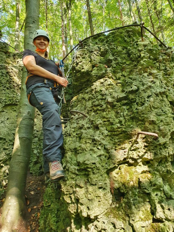 Ich stehe mit Kletterausrüstung an einem Felsen auf dem Bambini Klettersteig in der Fränkischen Schweiz. 