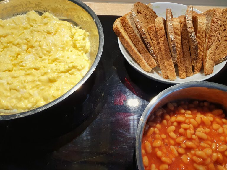 Eien Pfanne mit Rührei. Ein Teller mit Brot und Toast. Ein Topf mit gebackenen Bohnen.