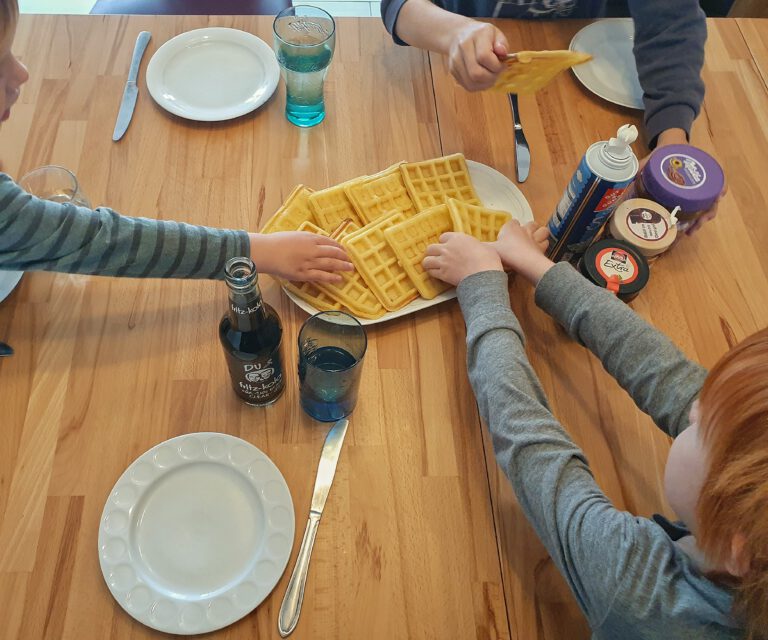 Viele Kinderhände die nach einem Teller voller Waffeln greifen.