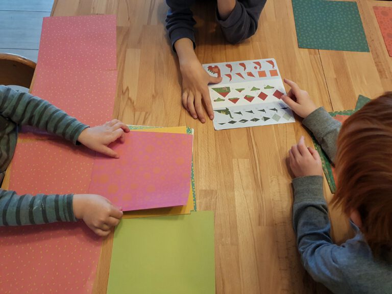 Drei Kinder und buntes Papier auf dem Tisch.