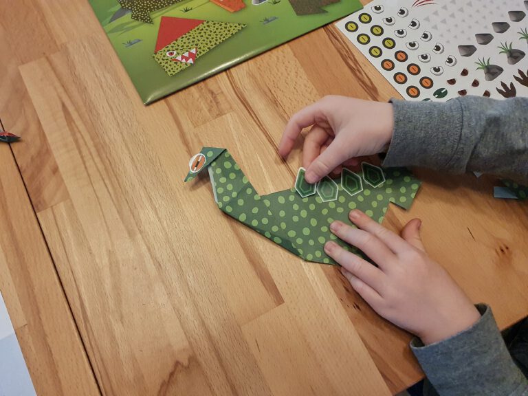 Kinderhände die einen Papier-Dinosaurier bekleben.