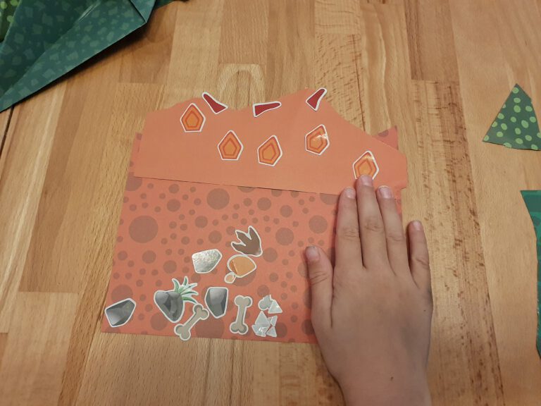 Eine Kinderhand die neben Papier und Stickern liegt.