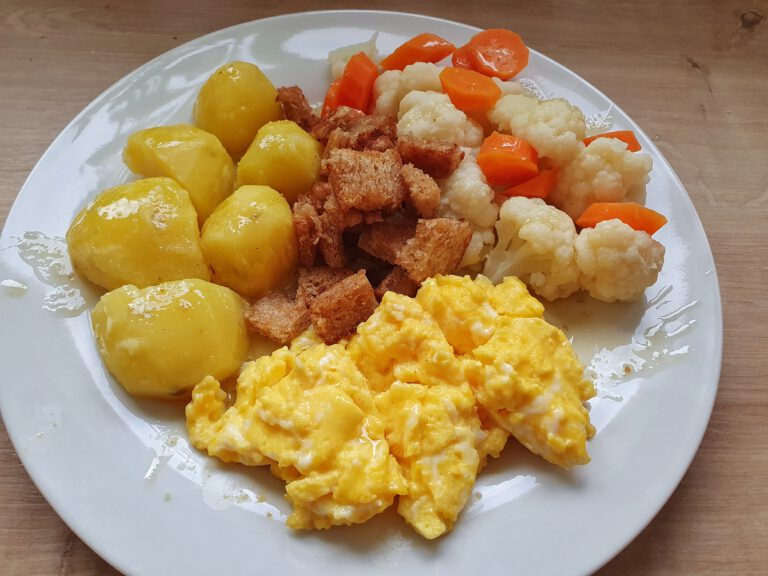 Ein Teller mit Kartoffeln, Blumenkohl, Möhren, Rührei und angebratenen Toast.