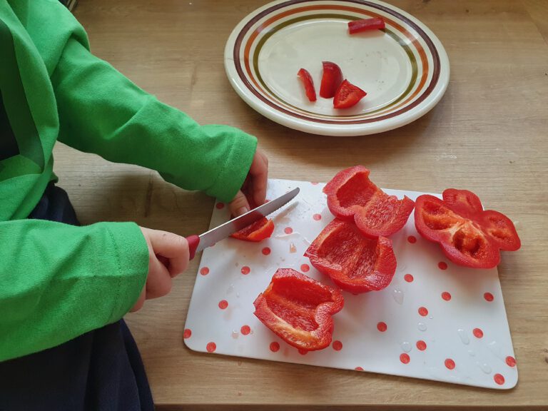 Zwei Kinderhände die eine rote Paprika schneiden.