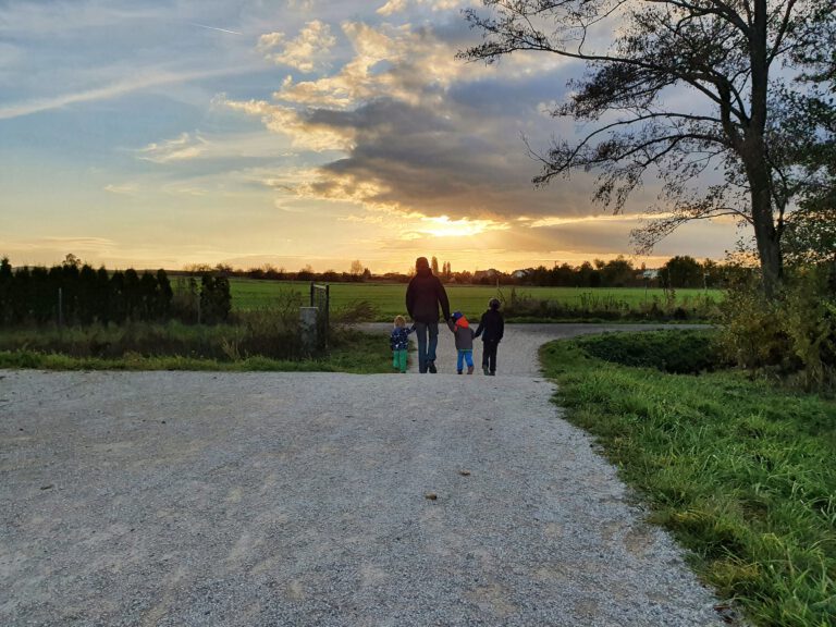 Drei Kinder und ein Erwachsener gehen Hand in Hand in die Abendsonne.