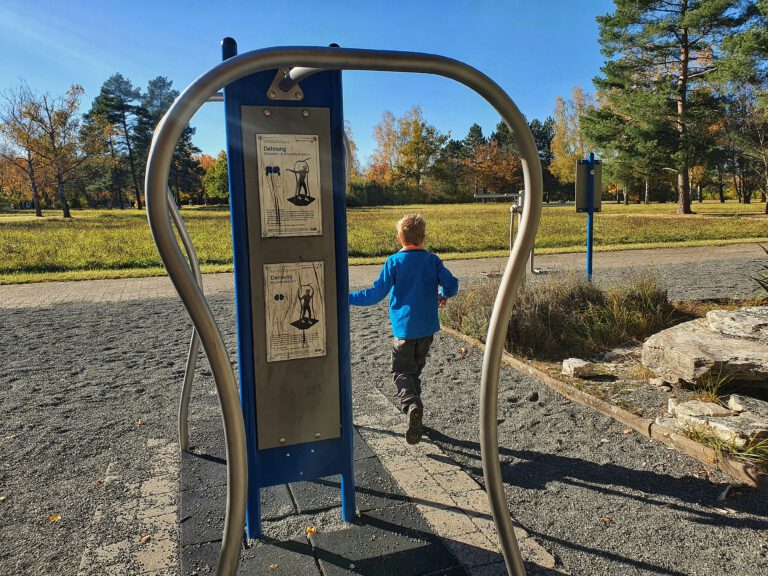 Ein Sportgerät auf einem Bewegungspark und ein Kind mit blauer Jacke.