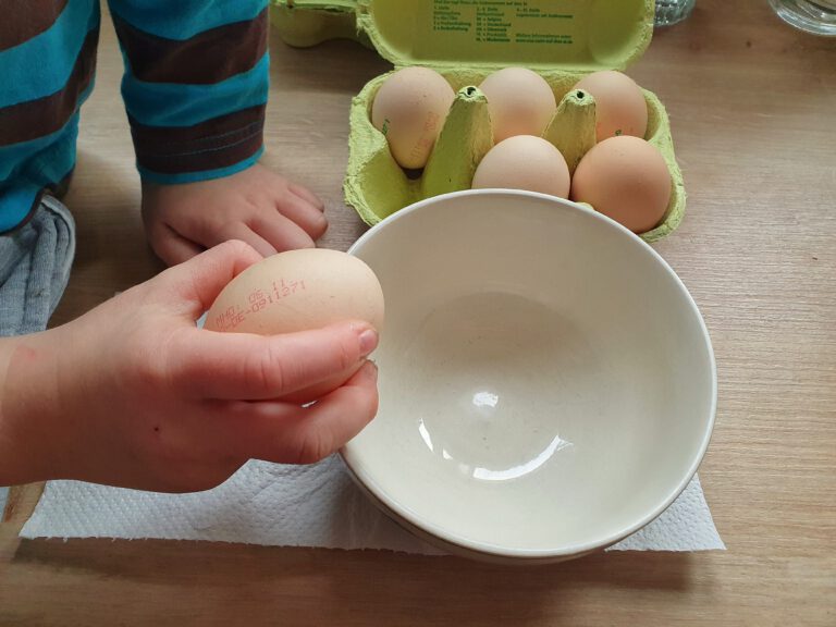 Ein Kind das ein Ei in eine Schüssel schlägt.