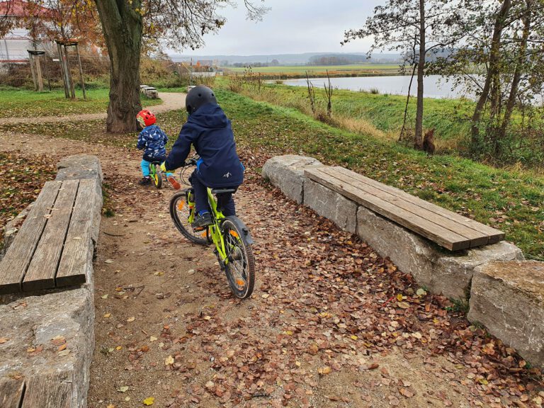 Ein kleines Kind auf einem Laufrad. Ein weiteres auf dem Fahrrad.