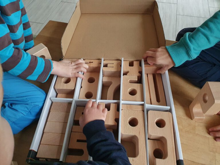 3 verschiedene Kinderhände greifen in eine Box mit Holzzahlen.