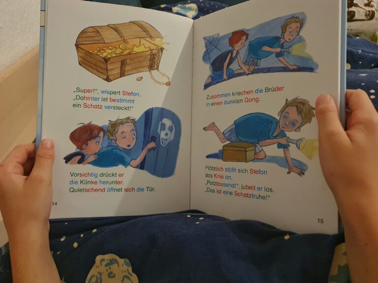 Kinderhände halten ein Silbenbuch.