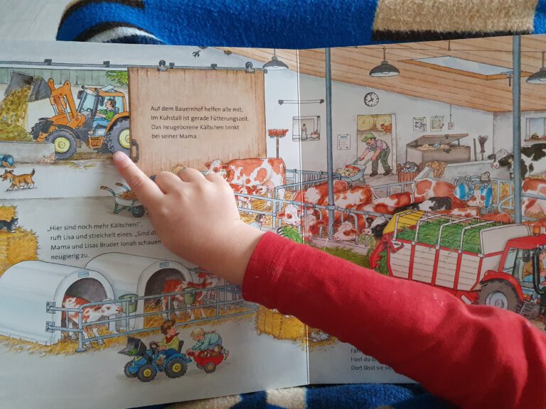 Eine Kinderhand die auf einen Traktor in einem Buch zeigt.