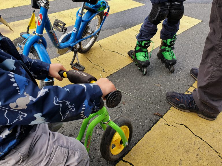 Ein Kinderfahrrad, ein Laufrad und ein Kind auf Inliner.