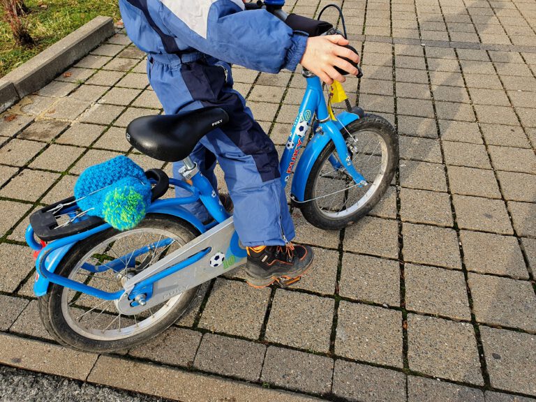 Ein blaues Kinderfahrrad mit einem Kind im blauen Schneeanzug.