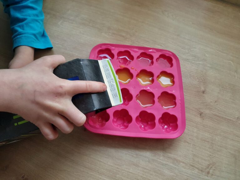 Kinderhände die einen Saft in eine Eiswürfelform füllen.