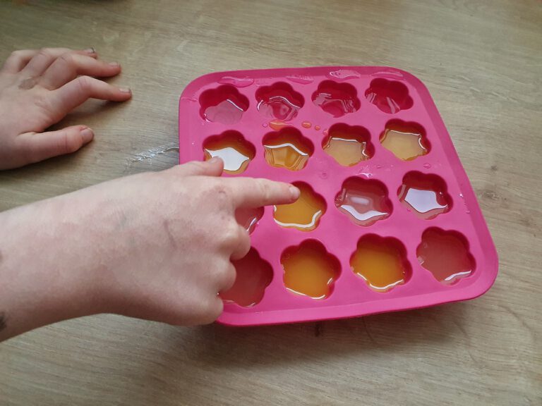 Kinderhände die auf die rosa Eiswürfelform zeigen.