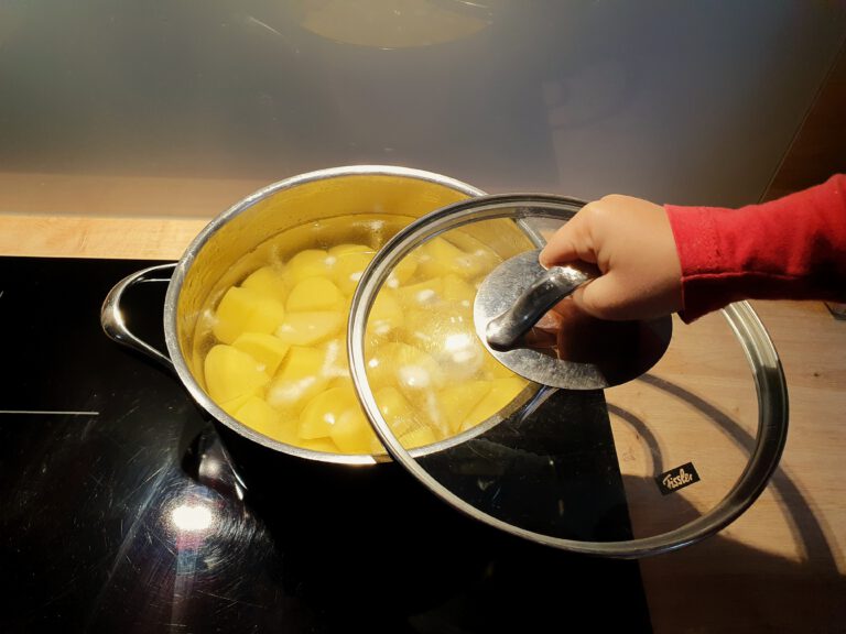 Eine Kinderhand die einen Deckel auf einen Topf Kartoffeln macht.