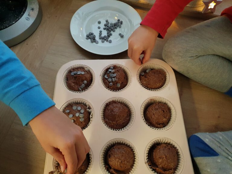 Kinderhände die Schokoladendrops auf einen Schokoteig verteilen.