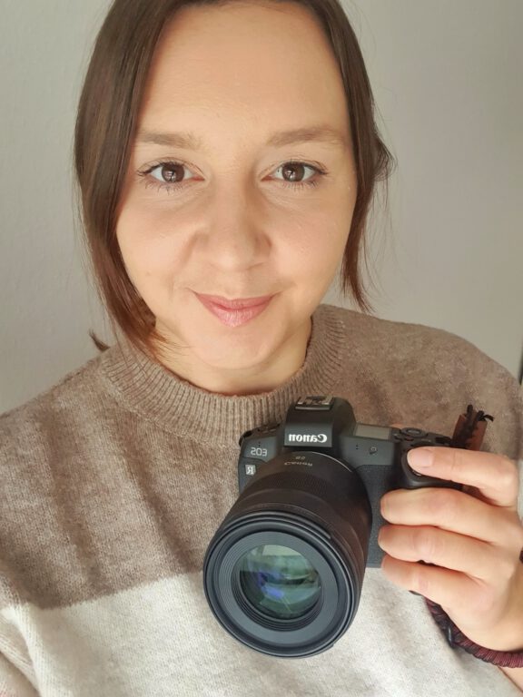 Ich schaue in die Kamera und habe eine schwarze Fotokamera in der Hand.