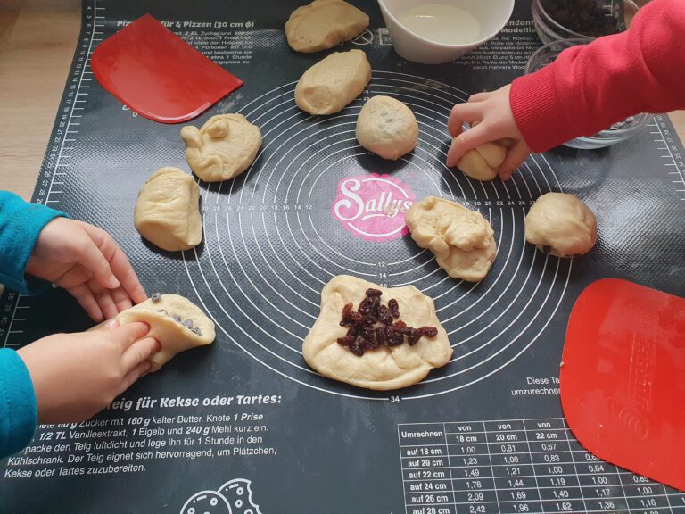 Vier Kinderhände arbeiten Schokodrops in einen Teig.