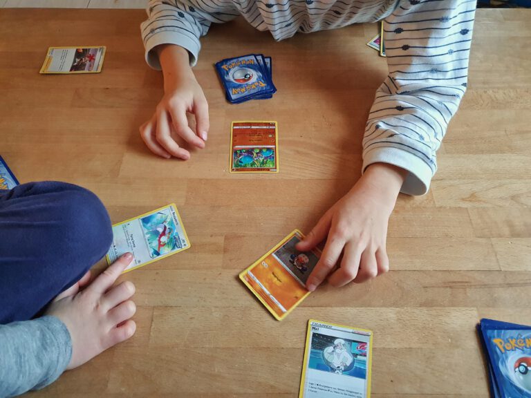 Kinderhände die mit Pokemonkarten spielen.
