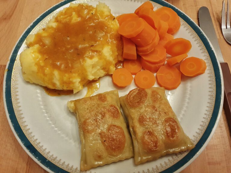 Ein Teller mit Kartoffelbrei und Soße, Möhren und Maultaschen.