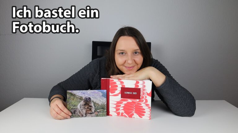 Ich lehne über einem rot weißen Fotobuch und habe ein Murmeltierfoto in der Hand.