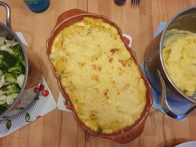 Ein gedeckter Tisch mit Kartoffelngratin und 2 Töpfen in der Mitte.