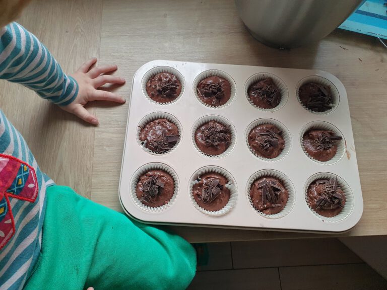 Ein Kind das neben einem gefüllten Muffinblech sitzt.