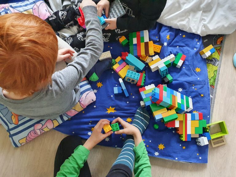 3 Kinder sitzen auf Decken und spielen mit Legosteinen,