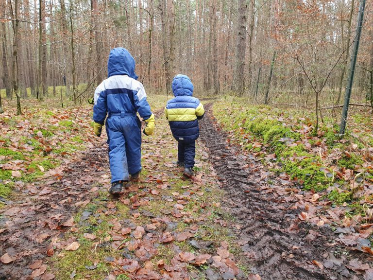 2 Kinder laufen warm eingepackt durch den Wald.