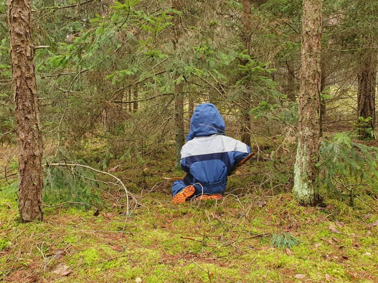 Ein Kind sitzt mitten im Wald und sammelt Holz.