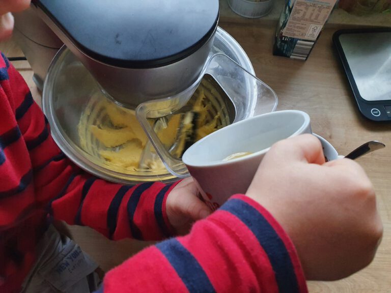 Kinderhände die eine Tasse an eine Küchenmaschine halten.