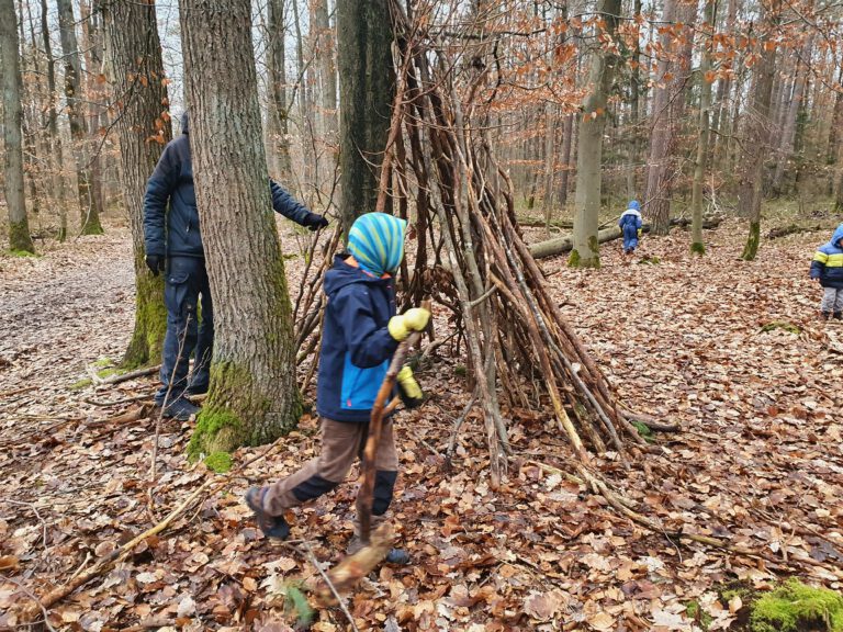 3 Kinder verstreut im Wald, die ein Tipi bauen.