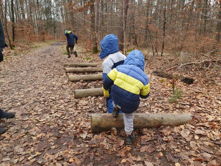 3 Kinder springen über Holzbalken.