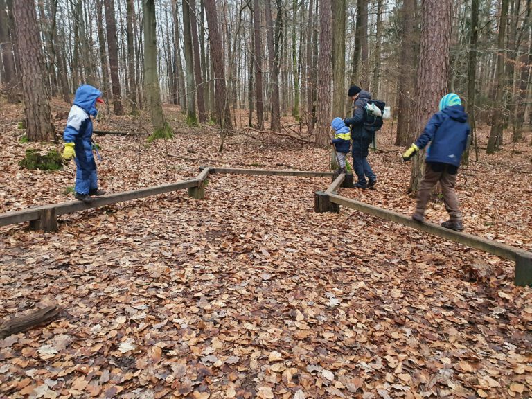 3 Kinder und ein Erwachsener balancieren auf Holzbalken.