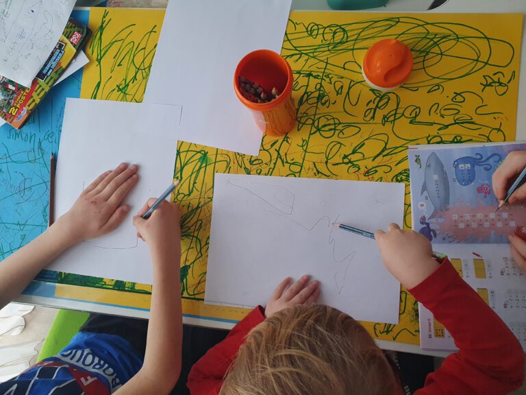 3 Kinder malen auf einem Schreibtisch.