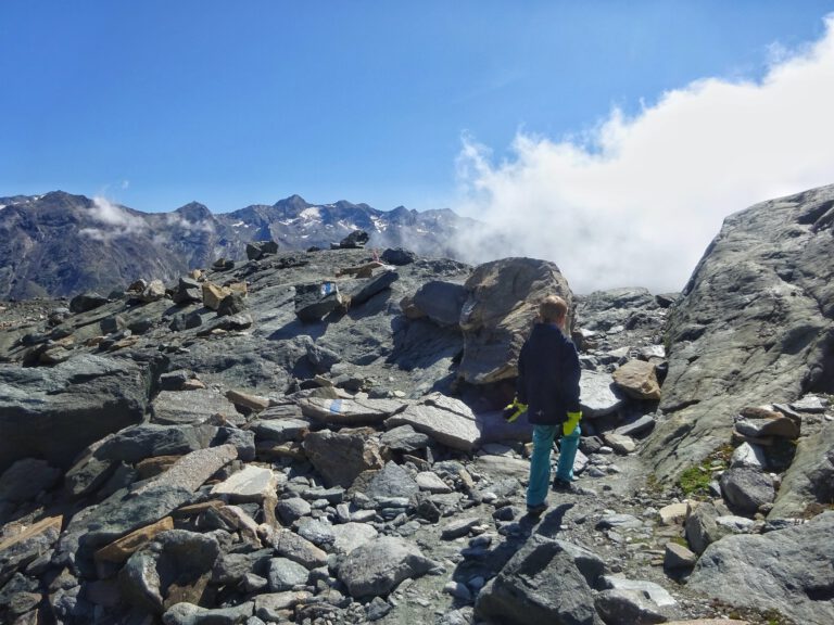 Ein Kind geht über einen Haufen Steine auf einem Berg in den Schweizer Alpen. Der Himmel ist blau und eine Wolke ist ganz nah.