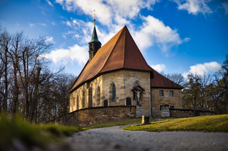 Eine Kirche mit Kreuz vorne. Der Himmel ist blau mit ein paar weißen Wolken.