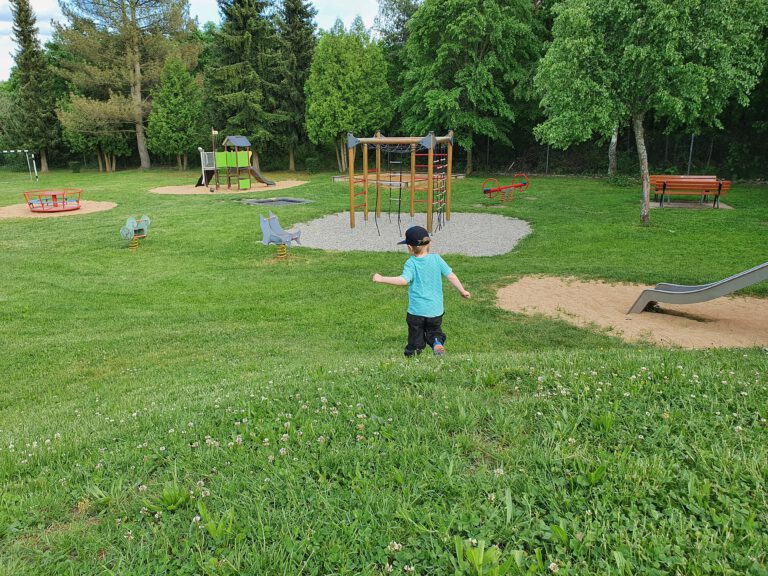 Ein Spielplatz auf dem ein kleines Kind einen Hügel runterläuft.