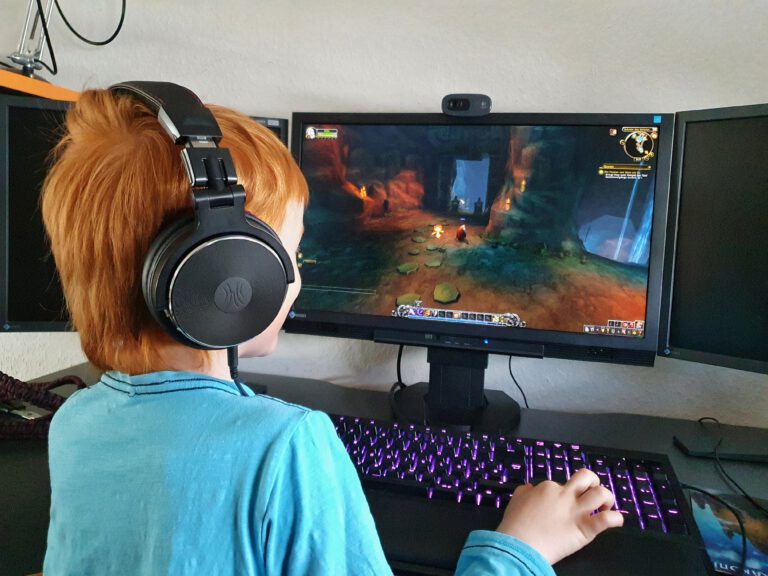 Ein rothaariges Kind mit Kopfhörern auf, welches das MMORPG World of Warcraft spielt.