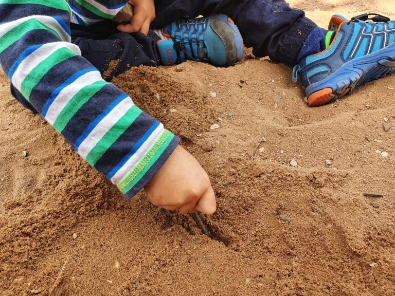 Eine kleine Kinderhand die im Sand buddelt.