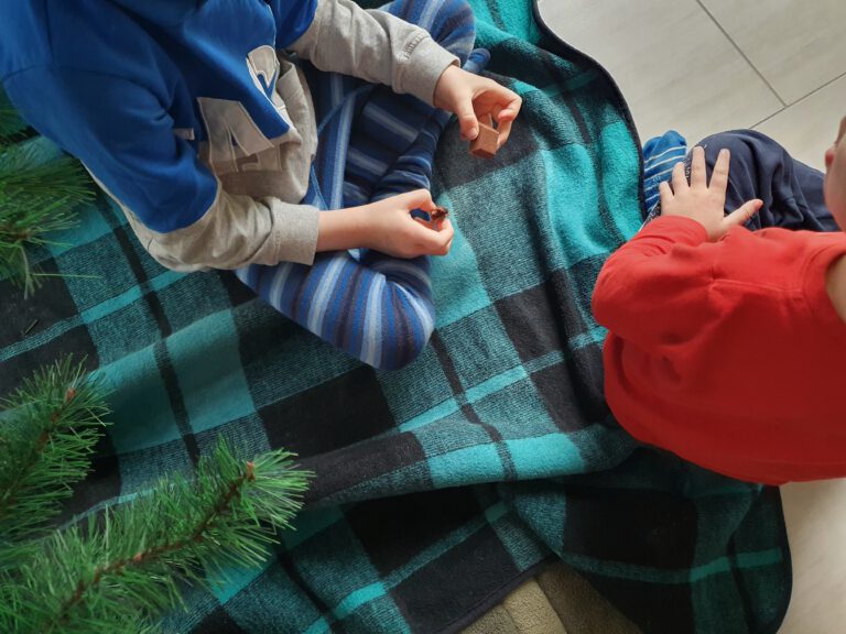 2 Kinder sitzen mit Schokolade unterm Weihnachtsbaum.